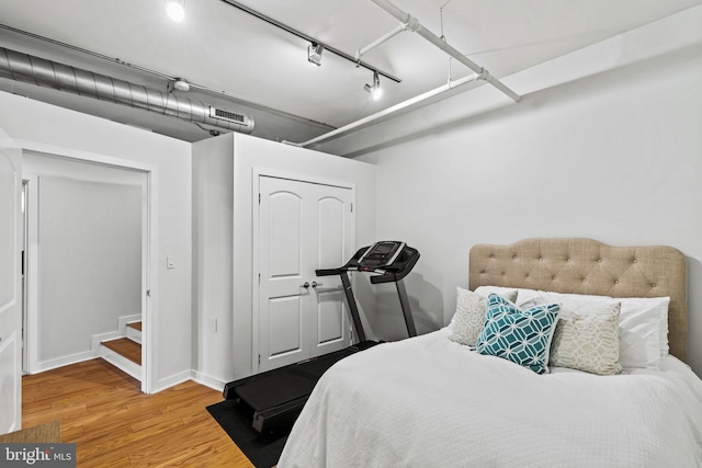 bedroom featuring wood finished floors, visible vents, baseboards, a closet, and rail lighting