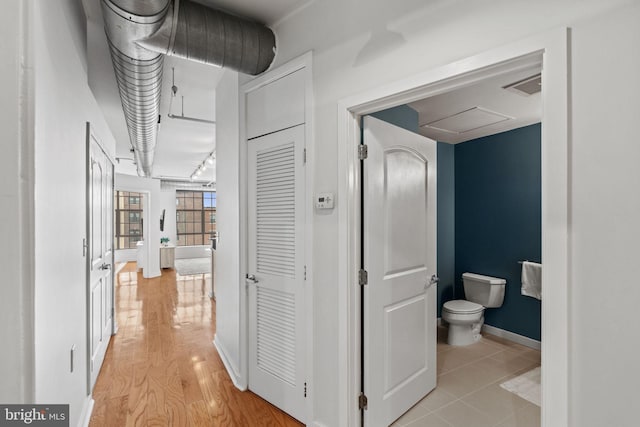 hallway featuring light wood finished floors, attic access, visible vents, and baseboards