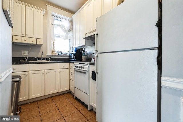 kitchen featuring dark countertops, under cabinet range hood, tile patterned floors, white appliances, and a sink