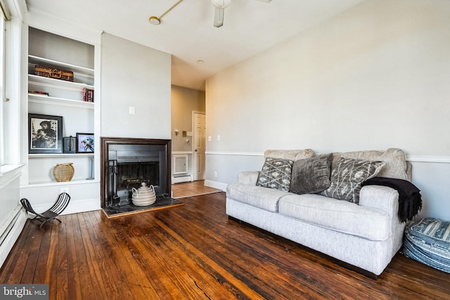 living area with a fireplace with raised hearth, built in shelves, a ceiling fan, and hardwood / wood-style flooring