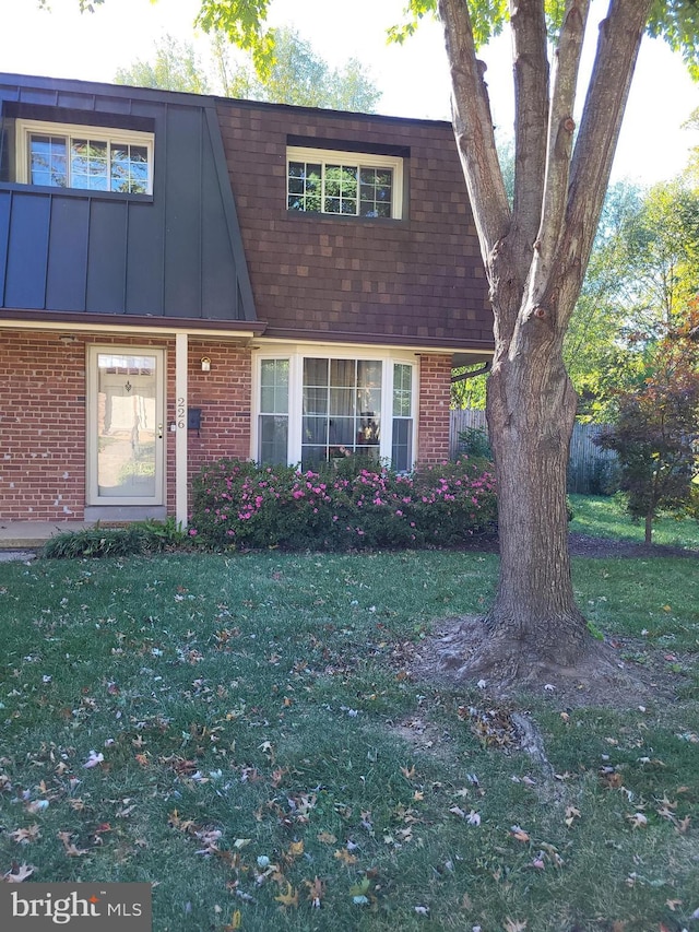 view of front of property featuring roof with shingles, brick siding, a front lawn, and board and batten siding