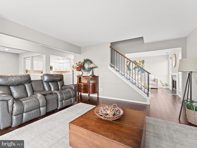 living area with a fireplace with flush hearth, dark wood-style flooring, stairway, and baseboards