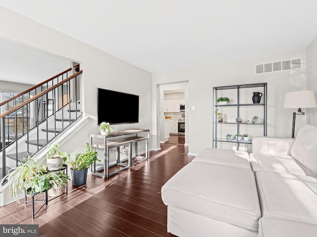 living area featuring dark wood-style floors, visible vents, baseboards, and stairs