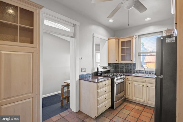 kitchen with gas stove, backsplash, sink, black fridge, and ceiling fan