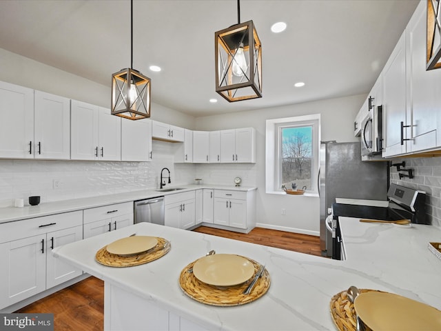 kitchen featuring white cabinetry, light stone countertops, sink, appliances with stainless steel finishes, and pendant lighting