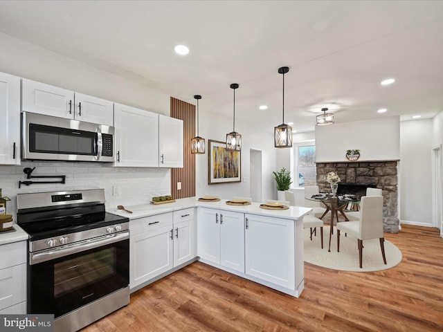 kitchen featuring light wood-type flooring, stainless steel appliances, kitchen peninsula, white cabinets, and hanging light fixtures