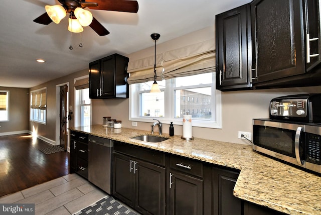 kitchen with light stone counters, appliances with stainless steel finishes, wood tiled floor, a sink, and baseboards