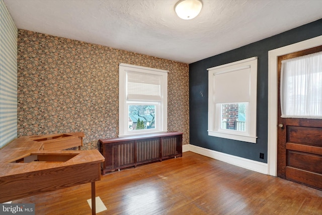 interior space featuring radiator, a textured ceiling, baseboards, and wood finished floors