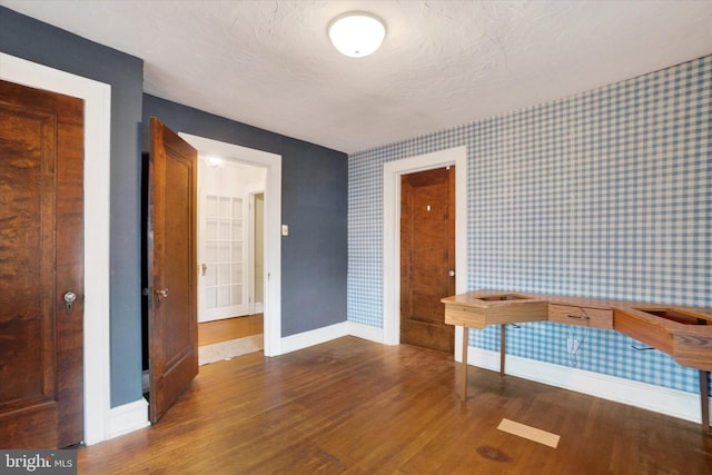 unfurnished room featuring baseboards, a textured ceiling, wood finished floors, and wallpapered walls