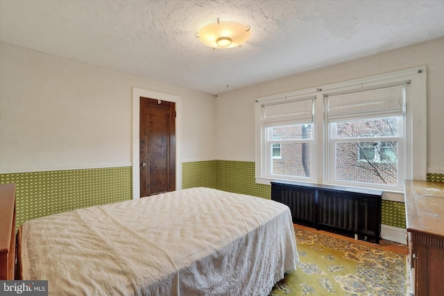 bedroom with a textured ceiling, radiator heating unit, and wainscoting