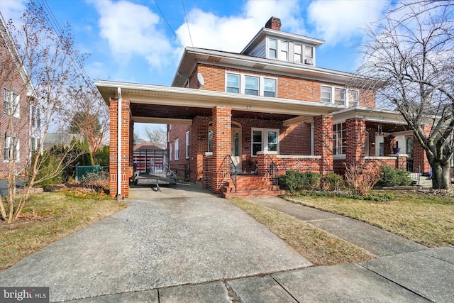 american foursquare style home featuring brick siding, a chimney, a porch, driveway, and a front lawn