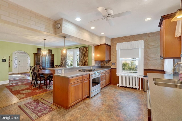 kitchen featuring stainless steel range with gas cooktop, brown cabinets, hanging light fixtures, radiator heating unit, and a sink