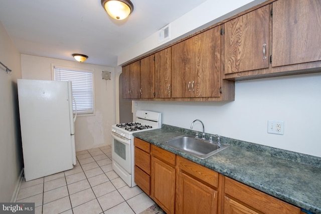 kitchen featuring light tile patterned flooring, white appliances, a sink, visible vents, and dark countertops