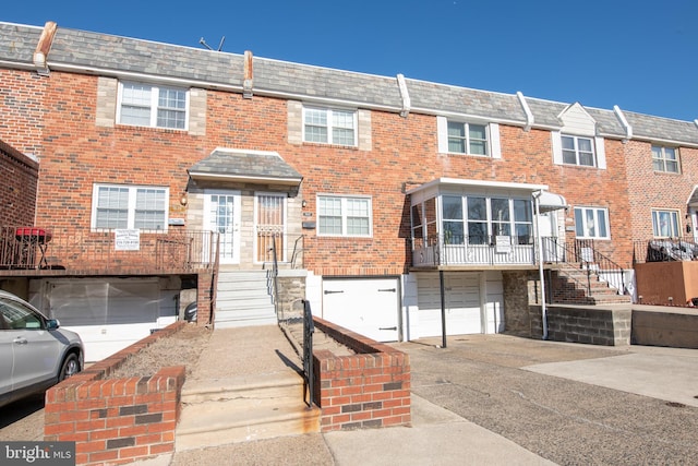 townhome / multi-family property featuring a garage, driveway, brick siding, and mansard roof