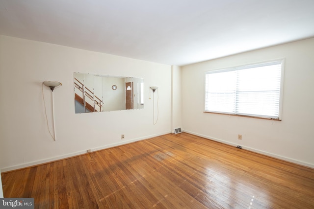 empty room featuring wood finished floors, visible vents, and baseboards