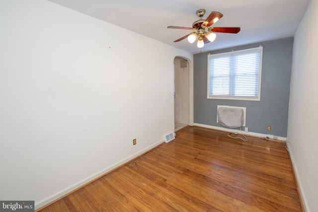 unfurnished room featuring arched walkways, light wood finished floors, visible vents, and baseboards