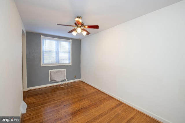 spare room featuring arched walkways, ceiling fan, light wood-style flooring, and baseboards