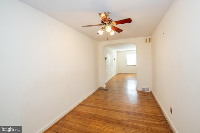 hall with arched walkways, visible vents, light wood-style flooring, and baseboards