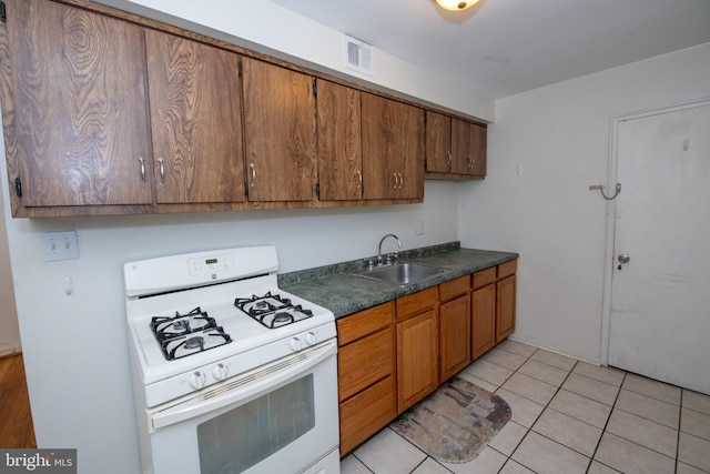 kitchen featuring brown cabinets, dark countertops, visible vents, a sink, and white gas range oven