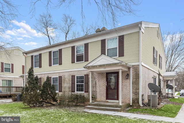 view of front of home with a chimney, a front lawn, central AC, and brick siding