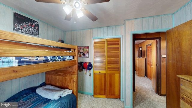 bedroom with wooden walls, a ceiling fan, and a closet