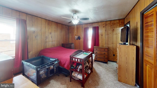 bedroom featuring light carpet, a ceiling fan, and wooden walls