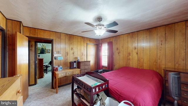 bedroom featuring ceiling fan, wooden walls, and light colored carpet