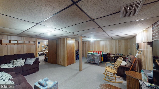 carpeted living area featuring a paneled ceiling, visible vents, and wooden walls