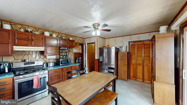 kitchen featuring stainless steel appliances, brown cabinets, under cabinet range hood, and wallpapered walls