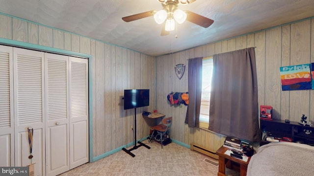 bedroom featuring a baseboard radiator, a closet, a ceiling fan, wood walls, and baseboards