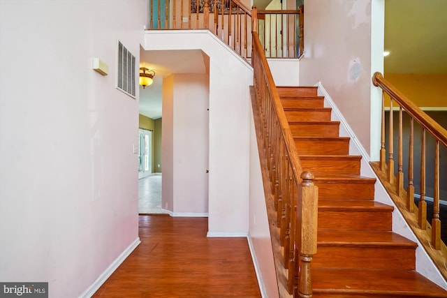 stairway with wood-type flooring and a high ceiling