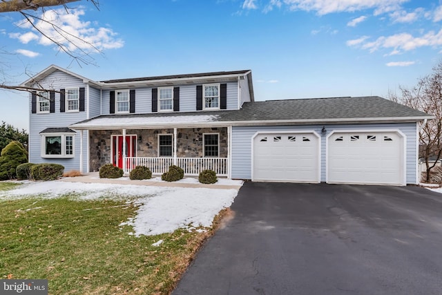 traditional-style house featuring aphalt driveway, covered porch, a garage, stone siding, and a front lawn