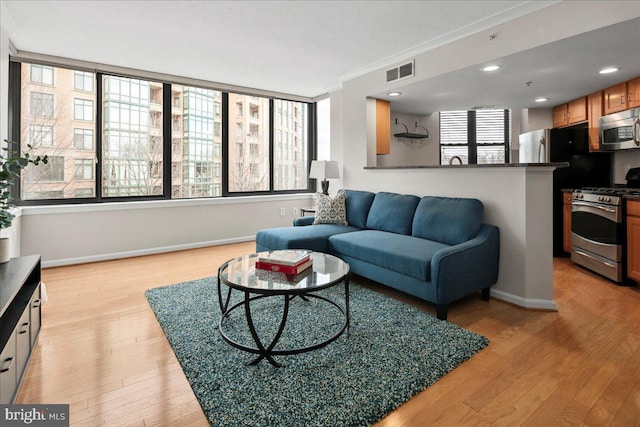 living area with baseboards, visible vents, crown molding, light wood-type flooring, and recessed lighting