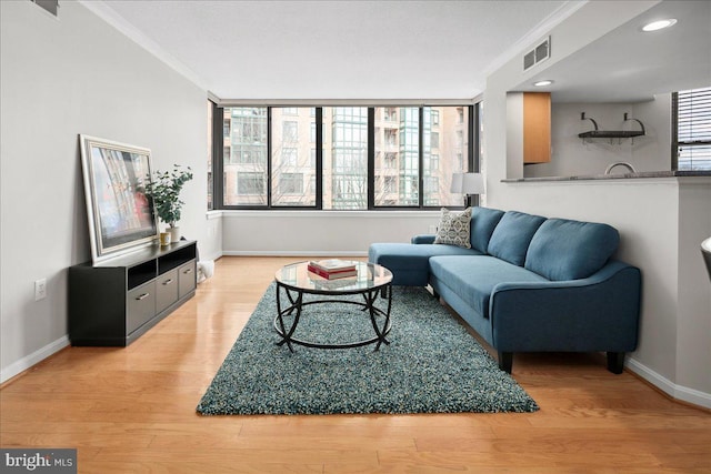 living room with ornamental molding, light wood-style flooring, visible vents, and baseboards