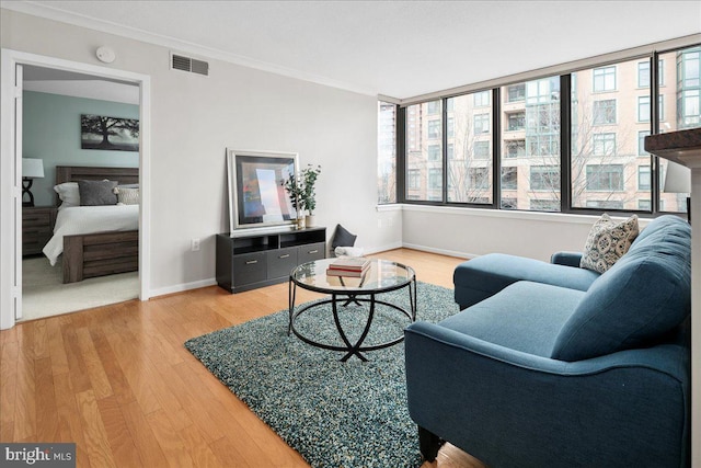 living area featuring baseboards, wood finished floors, visible vents, and crown molding