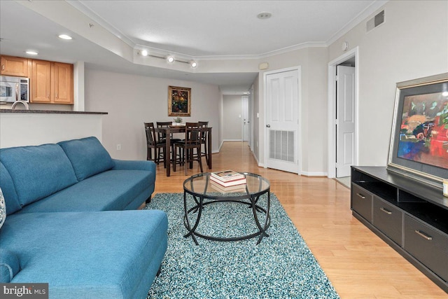 living area with ornamental molding, light wood-type flooring, visible vents, and baseboards