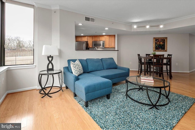 living area featuring light wood-type flooring, baseboards, visible vents, and ornamental molding