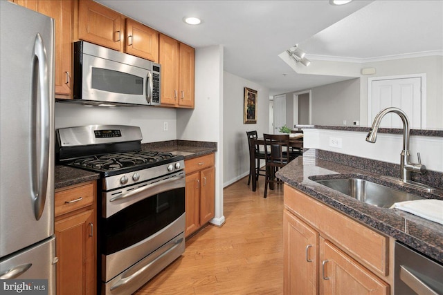 kitchen featuring dark stone counters, appliances with stainless steel finishes, brown cabinets, light wood-type flooring, and a sink