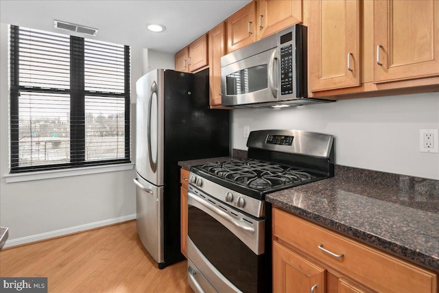 kitchen with stainless steel appliances, visible vents, light wood-style flooring, dark stone countertops, and baseboards