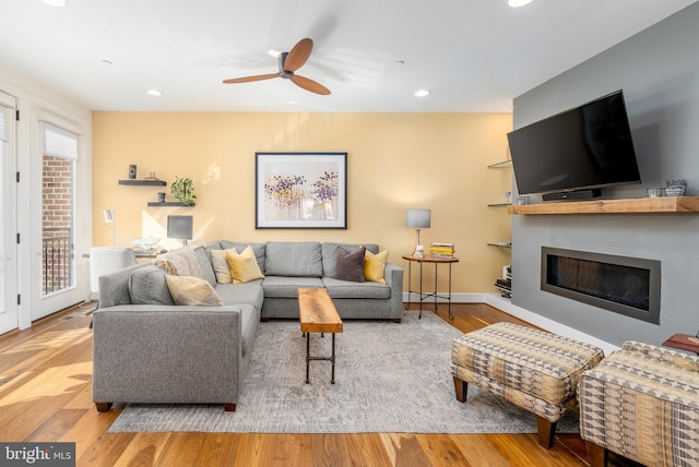 living area featuring light wood-style floors, a glass covered fireplace, a ceiling fan, and recessed lighting