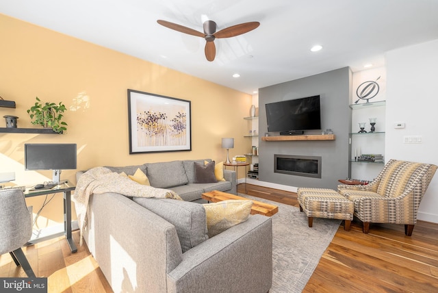 living area with recessed lighting, wood finished floors, a ceiling fan, baseboards, and a glass covered fireplace