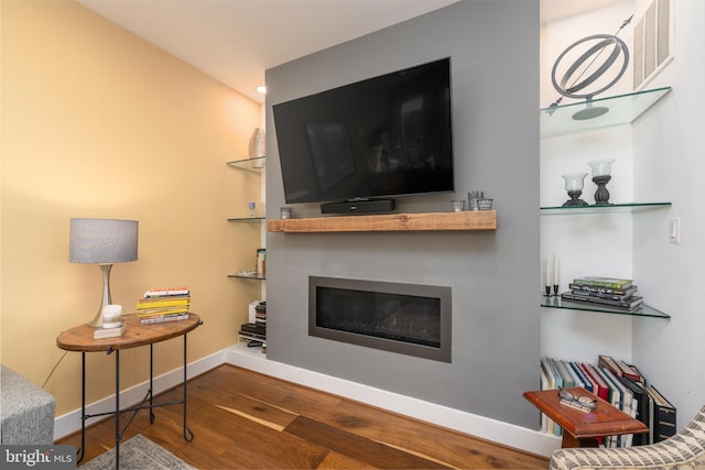 living room featuring a glass covered fireplace, dark wood finished floors, built in features, and baseboards