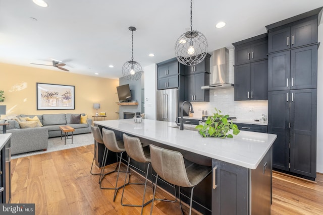 kitchen featuring pendant lighting, a large island, wall chimney exhaust hood, open floor plan, and a kitchen bar