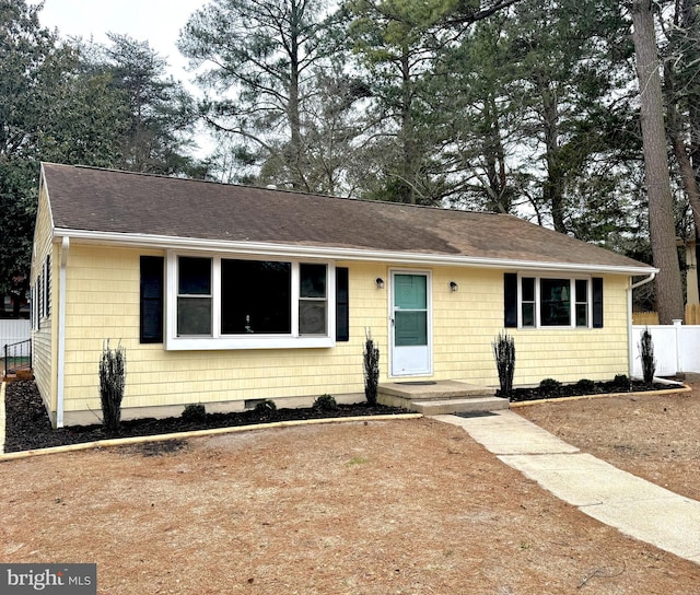 ranch-style house featuring a shingled roof and fence