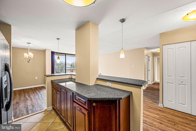 kitchen with fridge with ice dispenser, hanging light fixtures, light hardwood / wood-style floors, an inviting chandelier, and kitchen peninsula