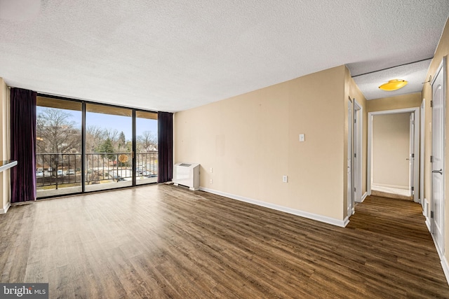 unfurnished living room with heating unit, dark wood-type flooring, floor to ceiling windows, and a textured ceiling