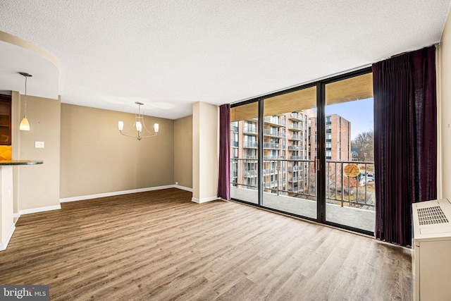 unfurnished room with hardwood / wood-style floors, a wall of windows, a notable chandelier, and a textured ceiling