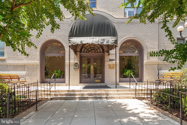 entrance to property featuring brick siding, fence, and french doors