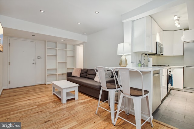 kitchen with light countertops, stainless steel microwave, white cabinets, light wood-type flooring, and a kitchen bar