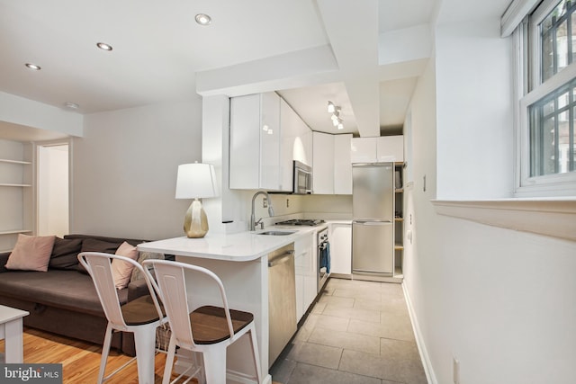 kitchen featuring light countertops, appliances with stainless steel finishes, white cabinets, a sink, and a kitchen breakfast bar